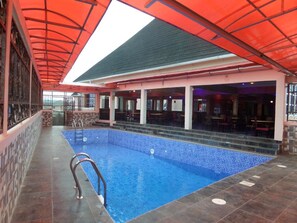 An indoor swimming pool with a tiled floor, surrounded by a covered area with tables and chairs. - De Zone Hotel (Lagos)