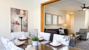 Comedor con mesa de vidrio, sillas blancas y un centro de mesa con planta.