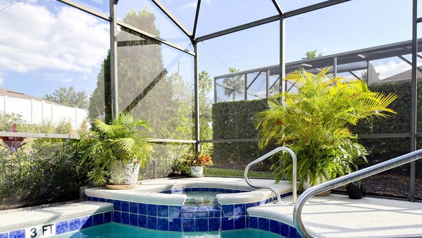 Una piscina con indicador de profundidad de 90 centímetros, rodeada de plantas en macetas y un cerramiento de vidrio.