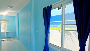 Una habitación con paredes azul claro, una ventana con cortinas azules y un techo blanco, con vistas al exterior con vegetación.