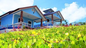 Un edificio azul con balcón y paneles solares, rodeado de vegetación verde.