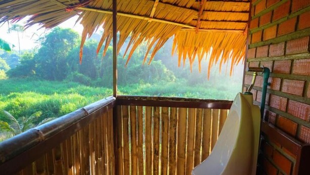 Una habitación con baranda de bambú, techo de paja y vista a exuberante follaje.