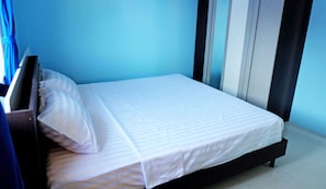 Ein Einzelbett mit weißer Matratze und Kissen in einem Zimmer mit blauen Wänden und einem dunklen Kopfteil.