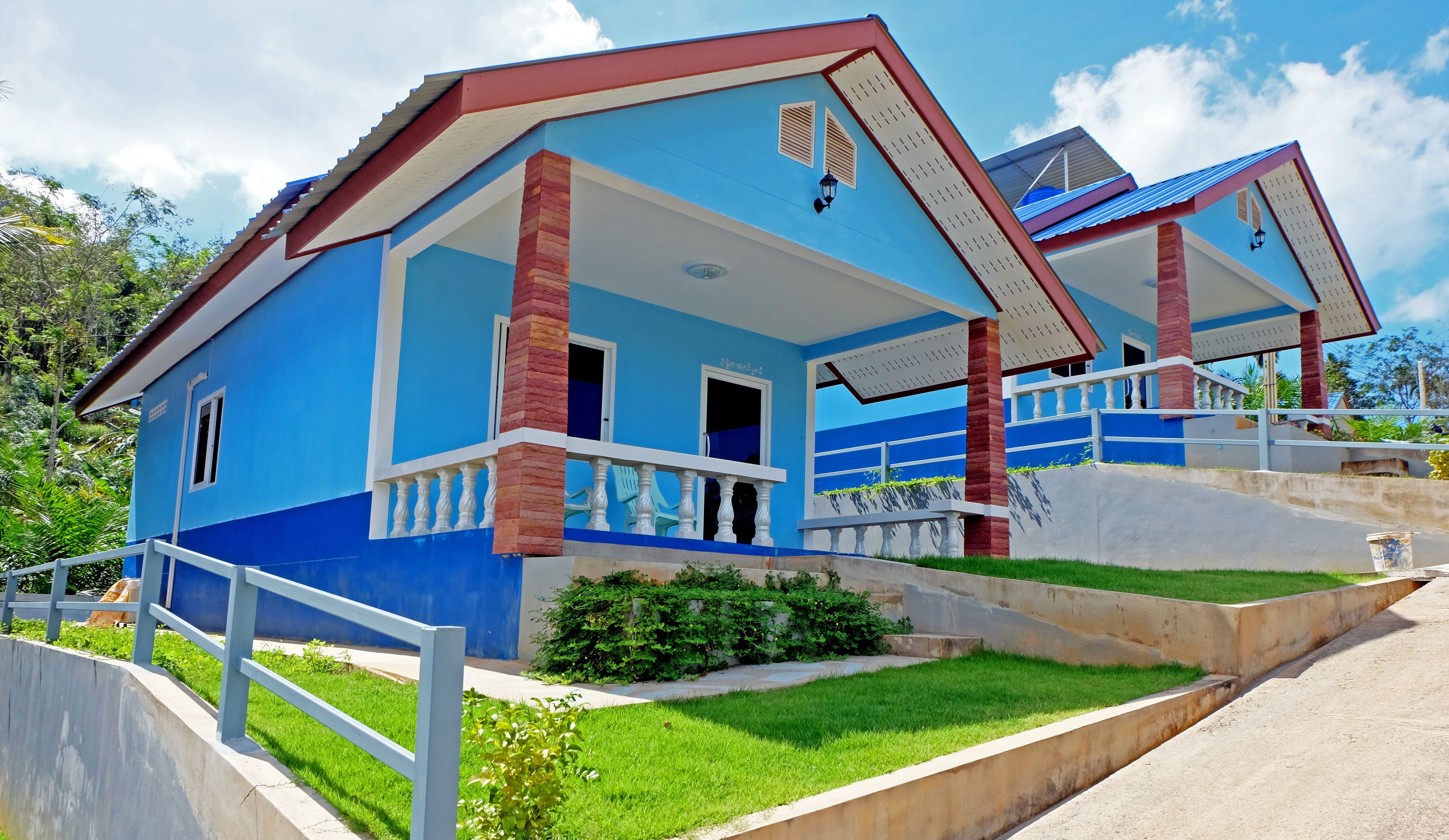 Una casa de dos pisos con fachada azul, barandillas de balcón blancas y techo rojo.