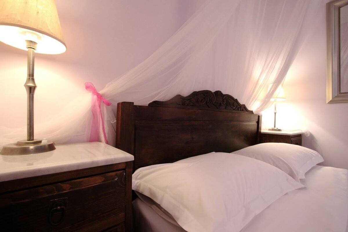 Ein ordentlich bezogenes Bett mit weißen Leinentüchern, einem Holzkopfbrett und einer Nachttischlampe.