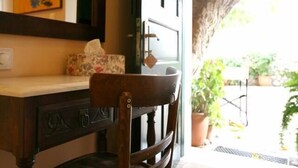 A wooden chair with a cushioned seat and backrest, positioned in front of a dark wooden desk with a mirror above it.
