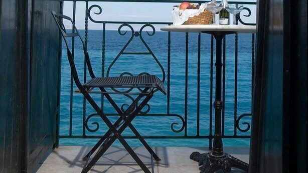 A balcony with a view of the sea, a chair, and a table with bottles.