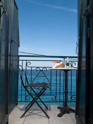 A balcony with a view of the sea, a chair, and a table with bottles. - Meliti Guesthouse (Aigialeia)