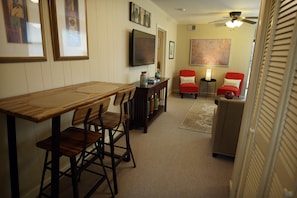 A dining area with a wooden table and chairs, a television mounted on the wall, and a ceiling fan.