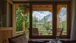 Un balcon en bois avec deux chaises et une table, d’où l’on peut admirer un paysage montagneux parsemé d’arbres et sur lequel se trouve un bâtiment.