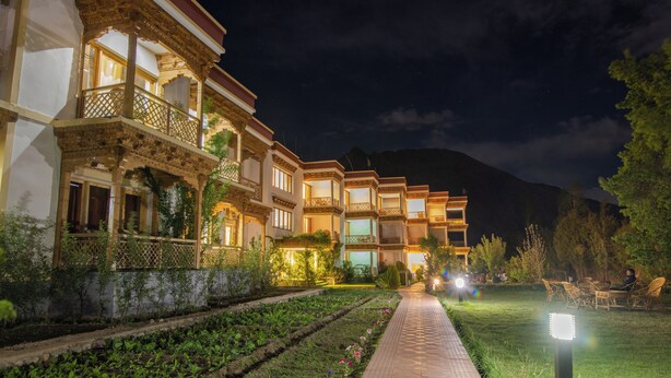 Un hôtel à plusieurs étages doté de balcons, d’un sentier bordé de jardins et offrant une vue sur les montagnes en arrière-plan.