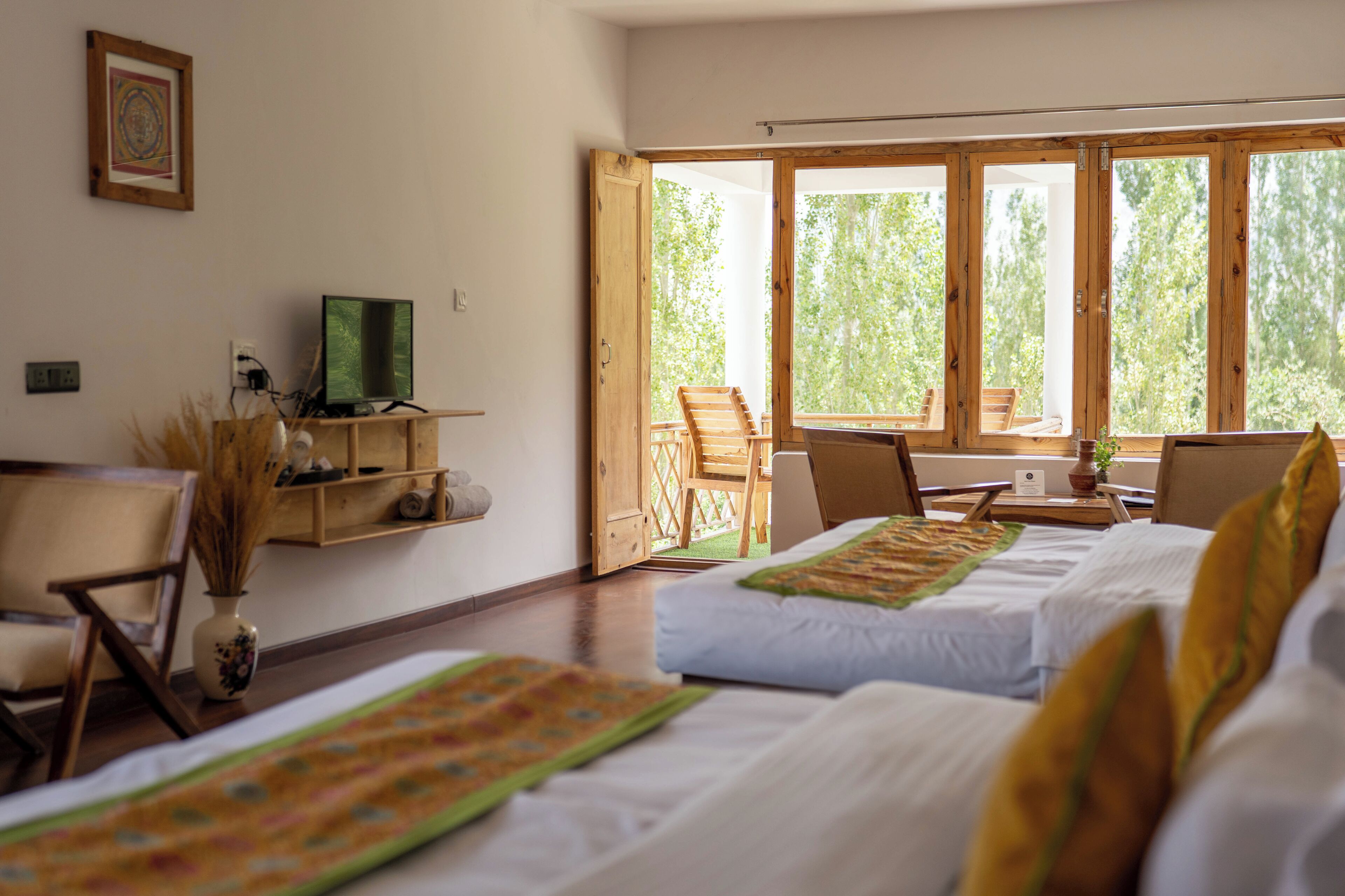 A room with two beds, a desk with a computer, a chair, and a window with a view of trees.