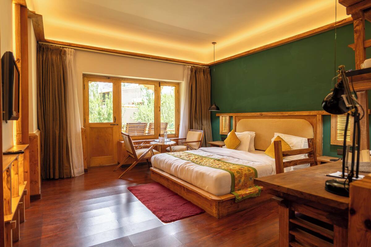 A bedroom with a wooden bed, a desk, a chair, and a view of the outdoors through a window.