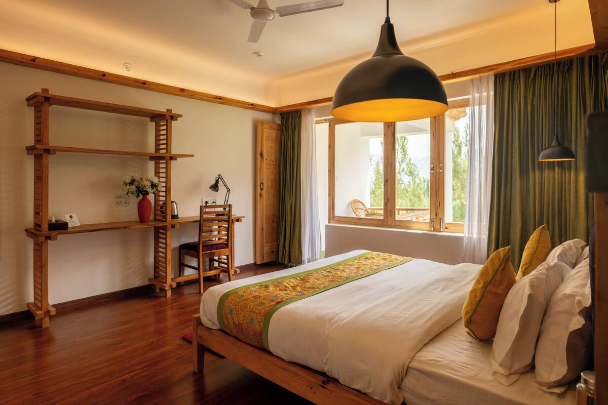 A bedroom with a wooden bed, a desk with a chair, a window with curtains, and a ceiling fan.