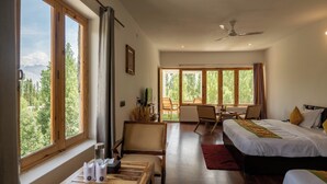 Une chambre d’hôtel moderne dotée d’un grand lit, d’un bureau avec une chaise et offrant une vue sur l’extérieur grâce à de grandes fenêtres.