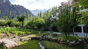Un paysage montagneux avec un petit ruisseau, une végétation luxuriante et des bâtiments modernes dotés de balcons.
