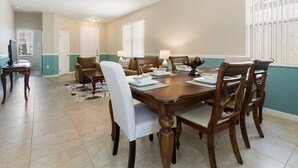 A dining area with a wooden table, chairs, and a vase. There is a door and a window with blinds in the background. - Modern pool home with Game Room, 2 en suites and just 15 minutes to Theme Parks! (Davenport)