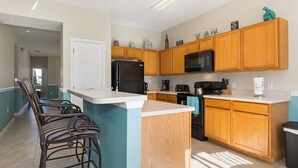 A kitchen with wooden cabinets, a black refrigerator, a microwave, and a coffee maker. There are two bar stools and a door leading to another room. - Modern pool home with Game Room, 2 en suites and just 15 minutes to Theme Parks! (Davenport)