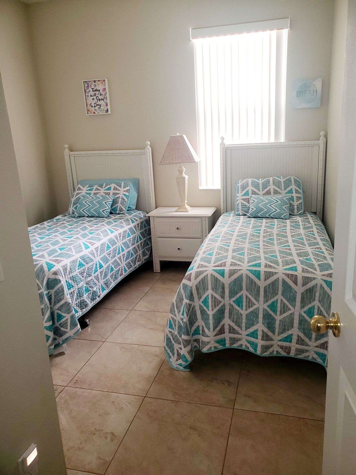 A bedroom with two beds, a nightstand, a lamp, and a window with blinds.