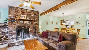 Ein Wohnzimmer mit Kamin aus Backstein, einer Couch, einem Holztisch und einem Essbereich mit Tisch und Stühlen.