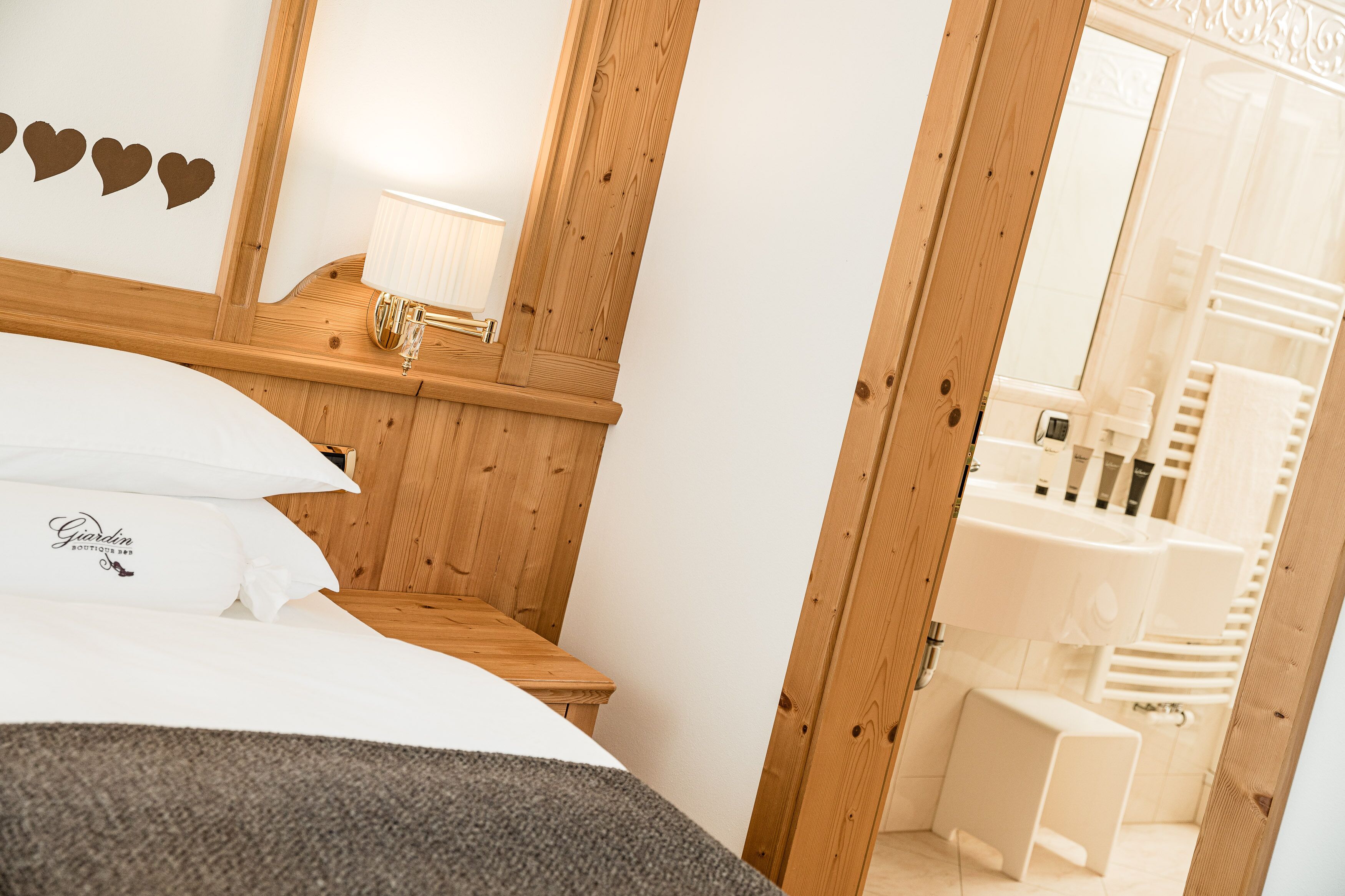 Ein Hotelzimmer mit einem hölzernen Kopfteil, einem Bett mit weißer Bettwäsche, einem kleinen Nachttisch mit Lampe und einem durch eine geöffnete Tür einsehbaren Badezimmer.