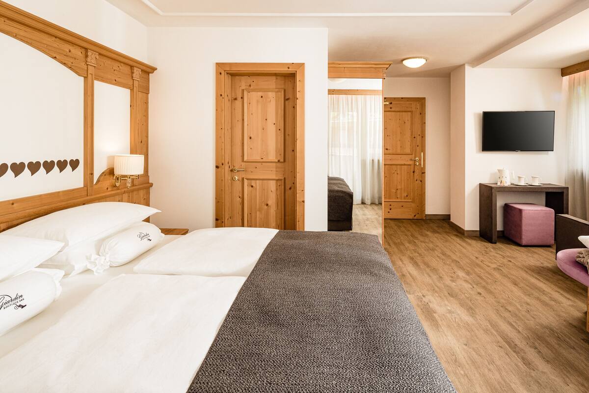 A hotel room with a large bed, a desk with a chair, a television, and a bathroom visible through an open door.