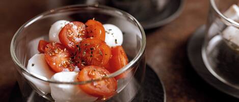 A clear glass bowl containing sliced tomatoes and mozzarella on a dark plate.