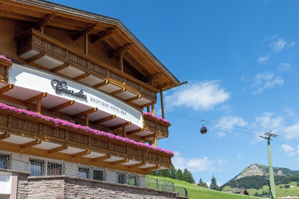 Un hotel con balcón adornado de flores, un letrero que indica que es un hotel boutique y un teleférico al fondo.