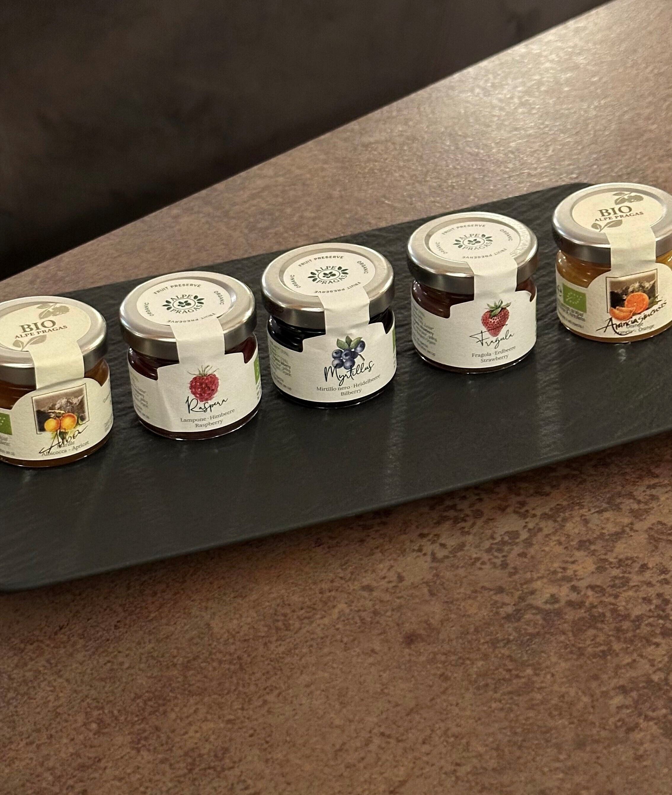 Cinq pots de fruits confits sur un plan de travail foncé.