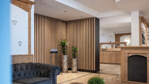 A modern lobby with a plush sofa, two large potted plants, and a wooden reception desk. - Giardin Boutique Hotel B&B (Selva di Val Gardena)