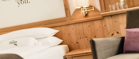 Una habitación de hotel con cabecera de madera, lámpara de noche, mesita de noche con cajón y cama con ropa blanca.