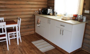 A compact kitchen with wooden walls, a white countertop, and a dining area with a white table and chair. - Dalia Barama (El-Rum)