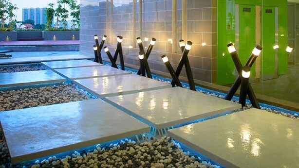 Un espace piscine intérieur moderne, doté de plusieurs couloirs de nage, d’un bordonnement de galets et d’un éclairage au plafond.