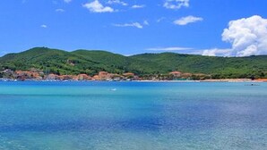 A coastal landscape with clear blue waters, green hills, and a distant mountain.