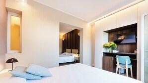A modern hotel room with a large bed, a desk with a chair, a TV, and a small kitchenette area.
