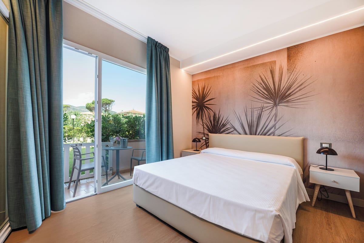 A bedroom with a large bed, a nightstand, a lamp, and a view of the outdoors through a sliding door.