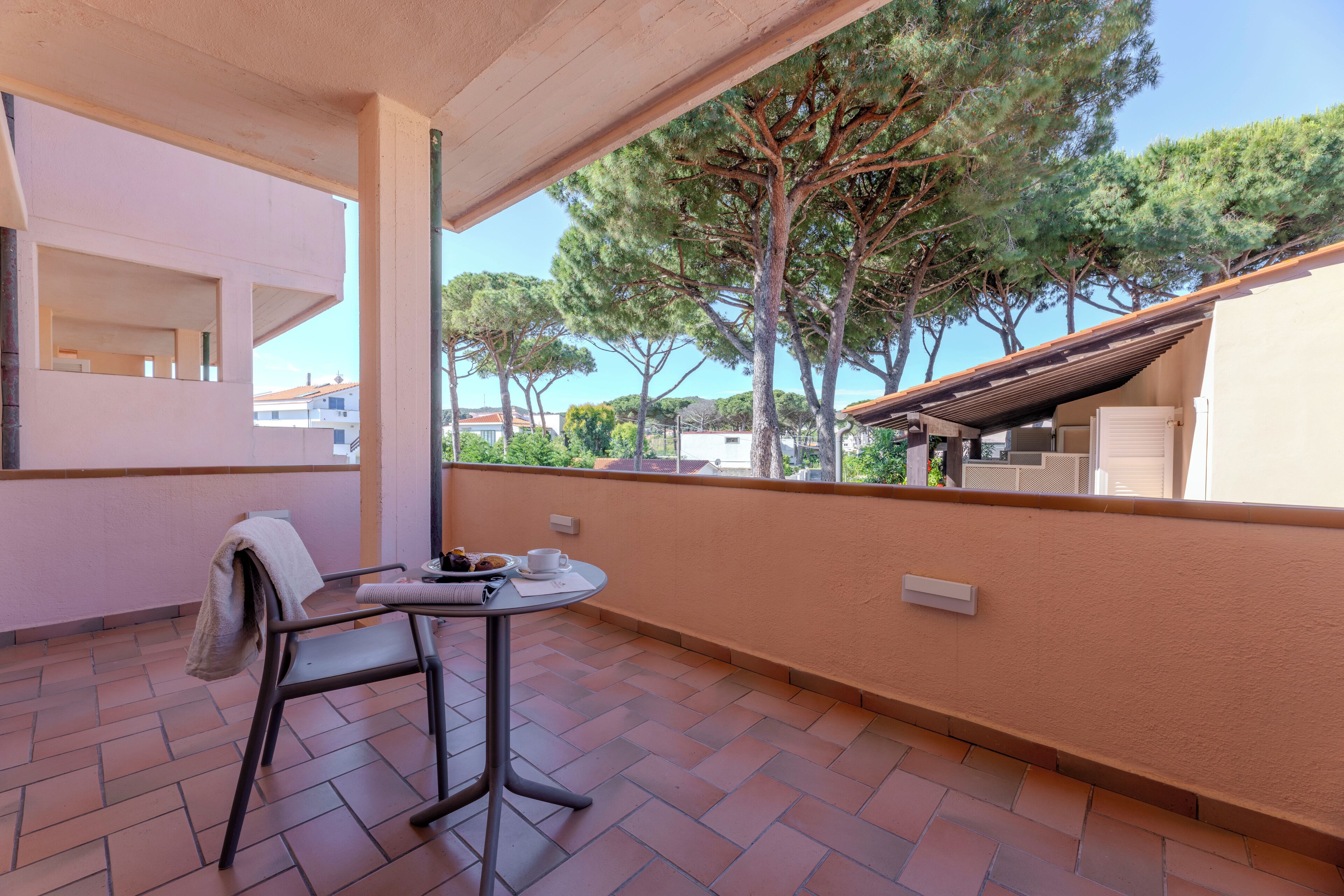 Un balcón con una mesa y una silla, con vistas a una zona residencial con árboles y casas.