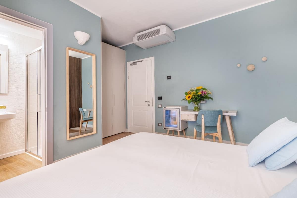 A bedroom with a large bed, a desk with a computer, a mirror, and a wall-mounted air conditioner.