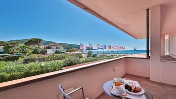A balcony with a table set for breakfast, overlooking a coastal area with flags and a view of the sea.
