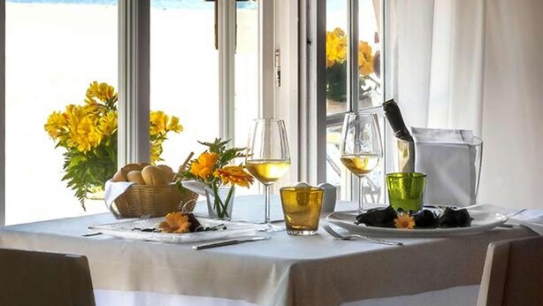 A table with a view of the beach, a bottle of wine, and a glass of wine on a table with a white tablecloth.