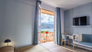 A room with a balcony, a TV mounted on the wall, a sofa, a small table with chairs, and a lamp.
