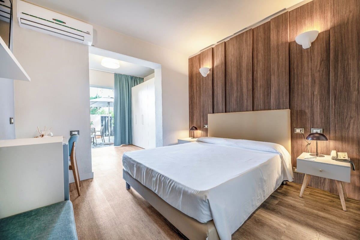 A modern bedroom with a large bed, bedside tables with lamps, a wardrobe, and an air conditioning unit.