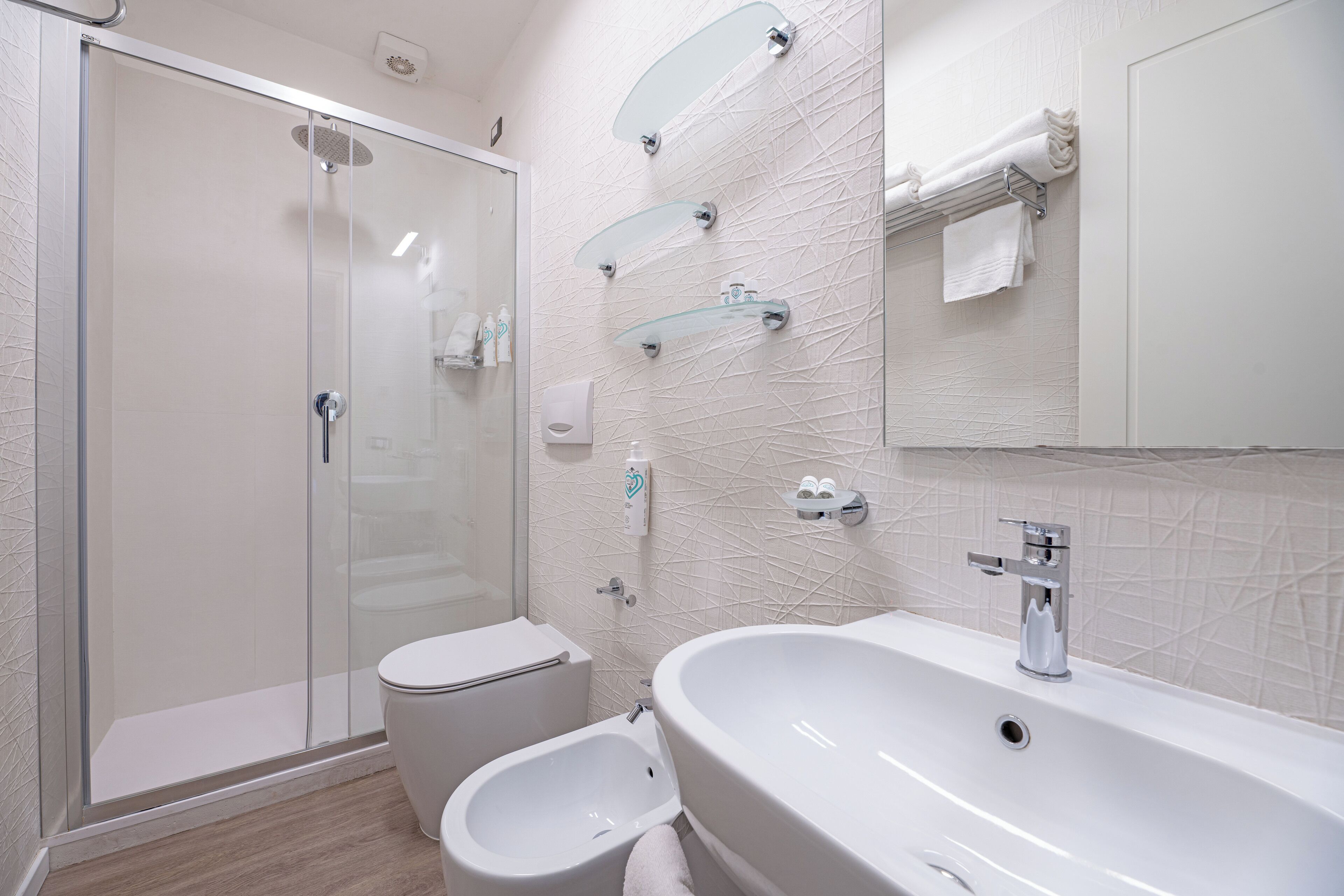 A modern bathroom with a glass-enclosed shower, a bidet, and a large sink with a mirror above.