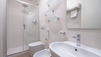 A modern bathroom with a glass-enclosed shower, a bidet, and a large sink with a mirror above.