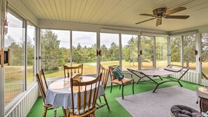 A covered patio with a table and chairs, a ceiling fan, and large windows offering a view of the outdoors. - Finger Lakes Retreat w/ Sunroom, Fire Pit & BBQ! (Himrod)
