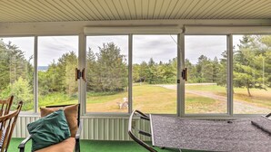 A room with large windows, a green carpet, a table, and a chair. - Finger Lakes Retreat w/ Sunroom, Fire Pit & BBQ! (Himrod)
