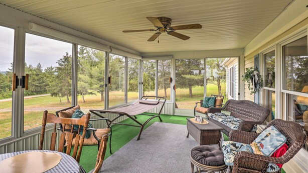 A covered porch with wicker furniture, a ceiling fan, and large windows offering a view of the outdoors. - Finger Lakes Retreat w/ Sunroom, Fire Pit & BBQ! (Himrod)