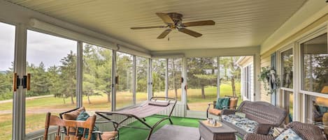 A covered porch with wicker furniture, a ceiling fan, and large windows offering a view of the outdoors.