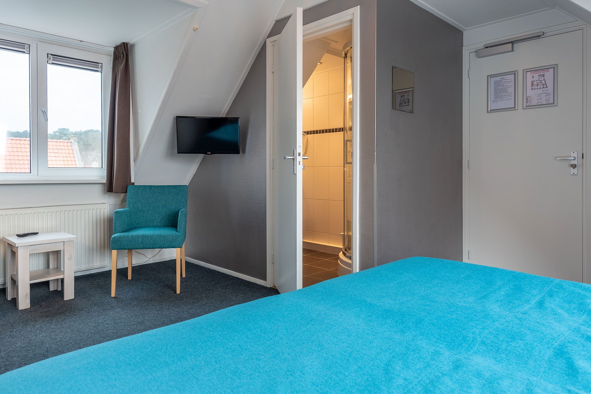 Een slaapkamer met een bed, een stoel, een televisie en een badkamer.