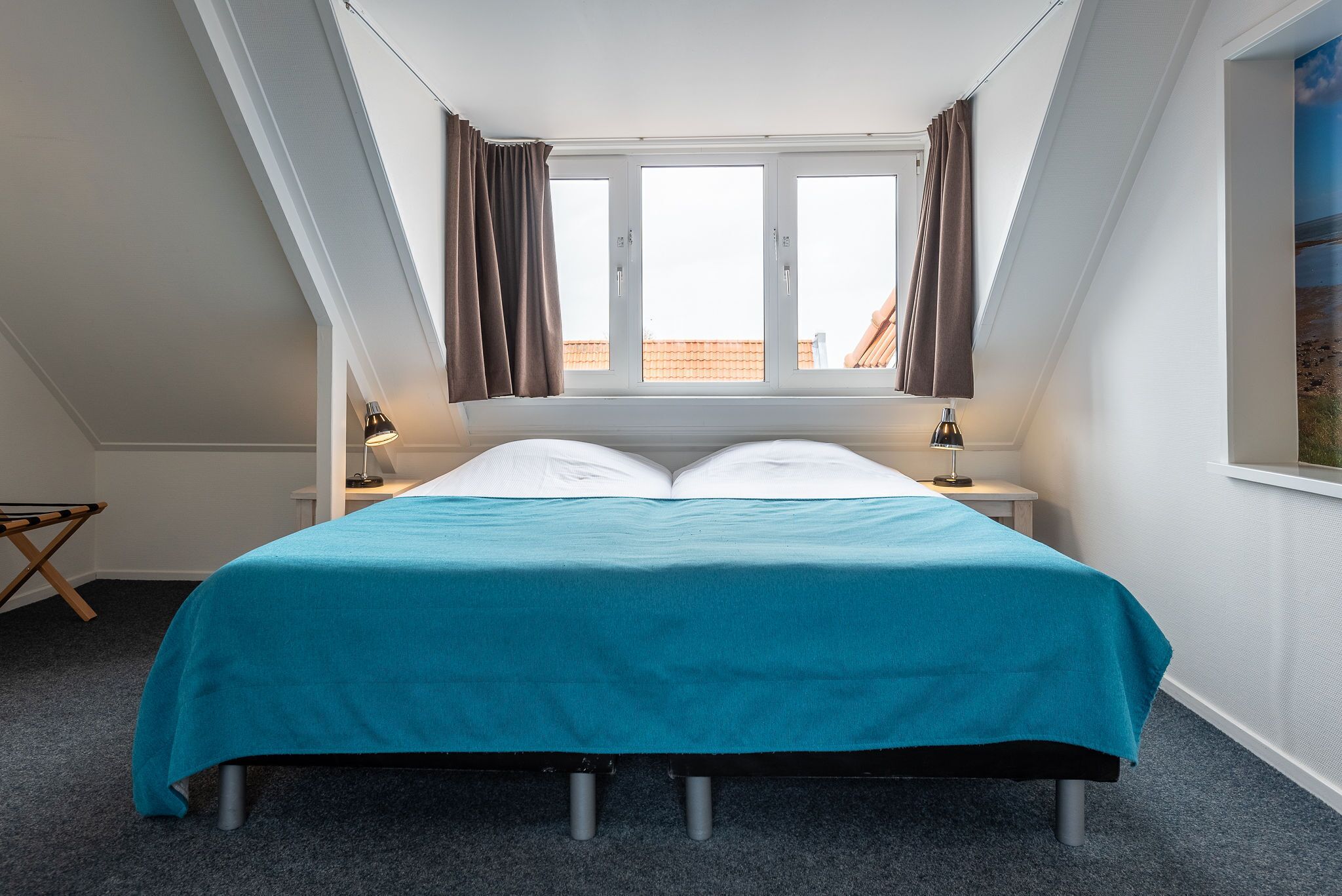 A bedroom with a bed, two bedside tables, a window with curtains, and a view of the outside.